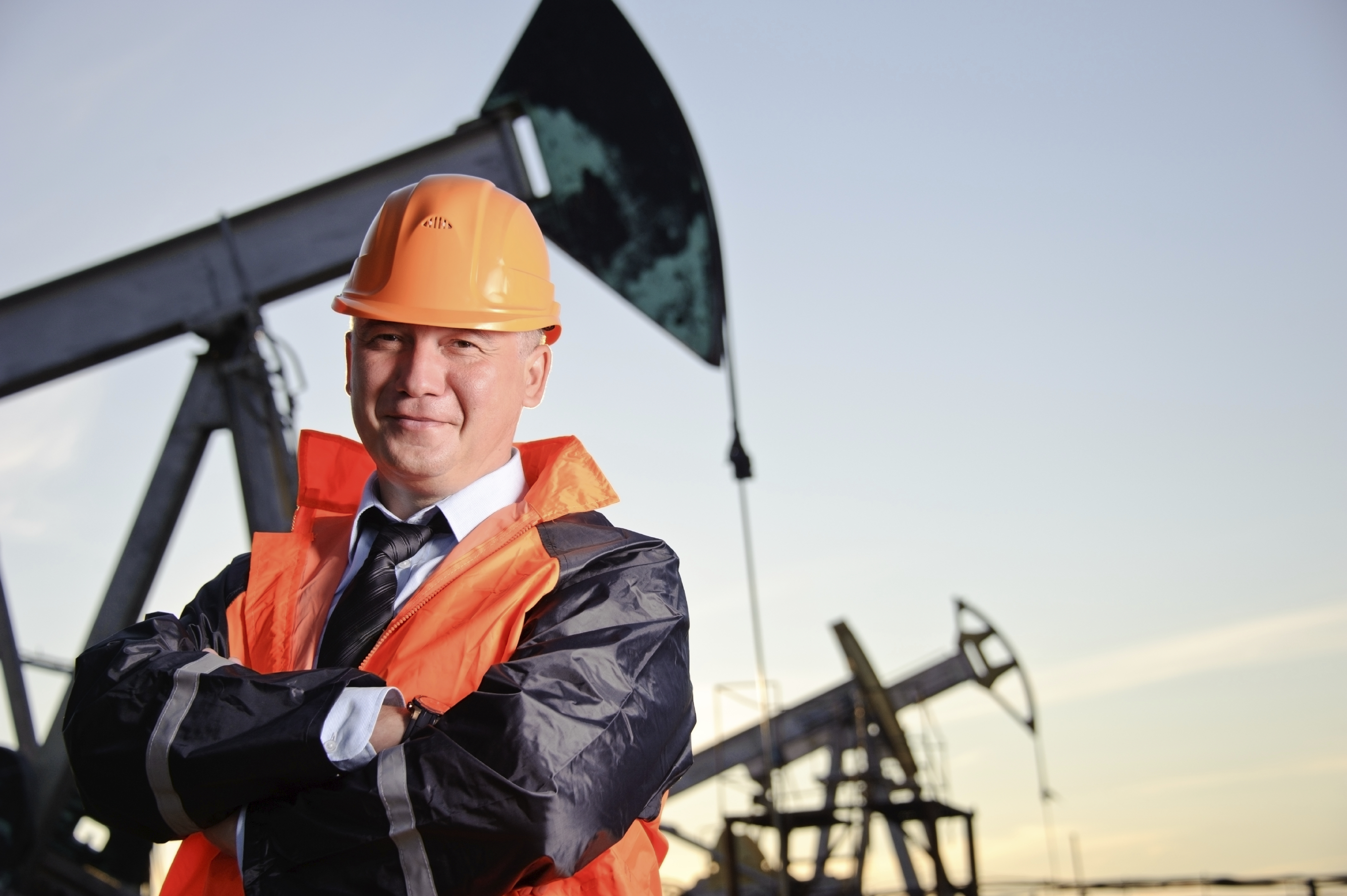 Oil worker in orange uniform and helmet on of background the pump jack and sunset sky.